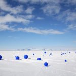 Docenas de esferas azules ultramarinas brillantes se extienden al azar a través de hielo polar debajo de un cielo azul brillante