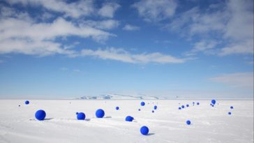 Docenas de esferas azules ultramarinas brillantes se extienden al azar a través de hielo polar debajo de un cielo azul brillante