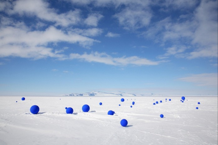 Docenas de esferas azules ultramarinas brillantes se extienden al azar a través de hielo polar debajo de un cielo azul brillante