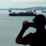 A tourist looks at a cargo ship sailing through the Agua Clara Locks of the Panama Canal